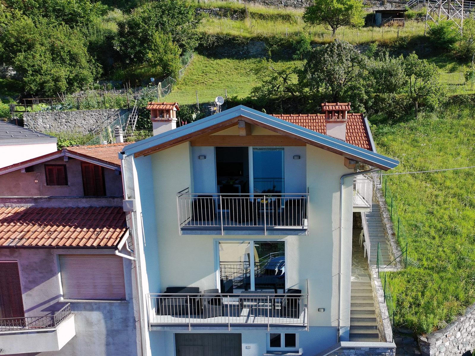 Zweistöckiges Haus mit Balkonen und Terrasse auf grüner Hanglage.