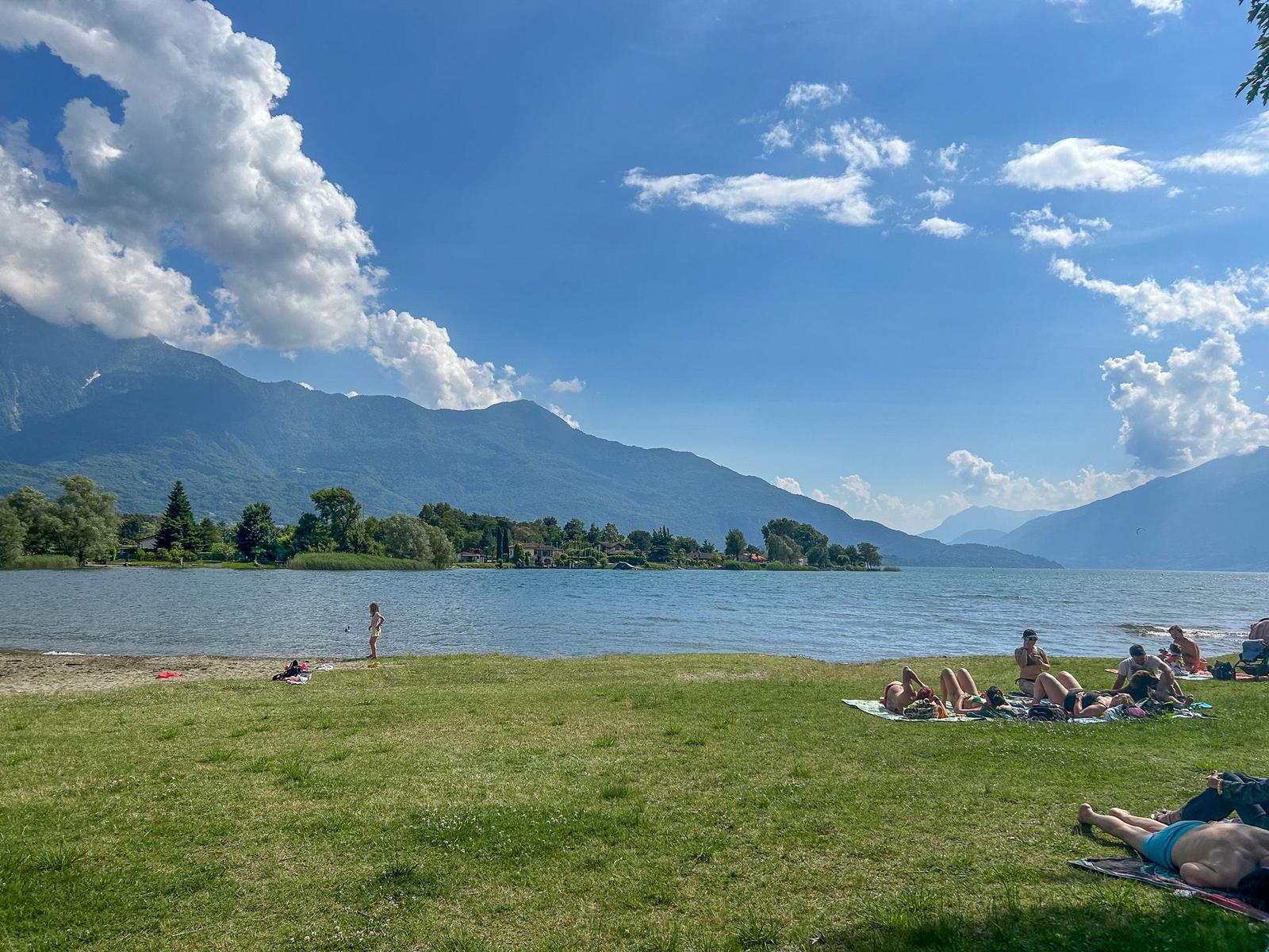Grüner Strand mit Menschen, die sich sonnen, und Bergen im Hintergrund.