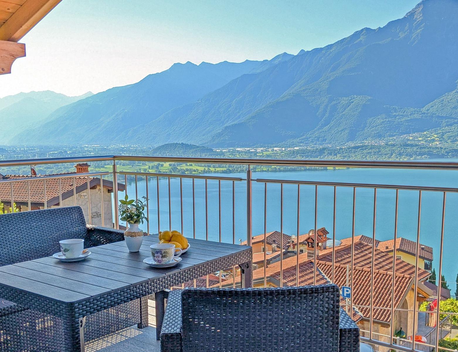Terrasse mit Tisch und Stühlen, Blick auf See und Berge.