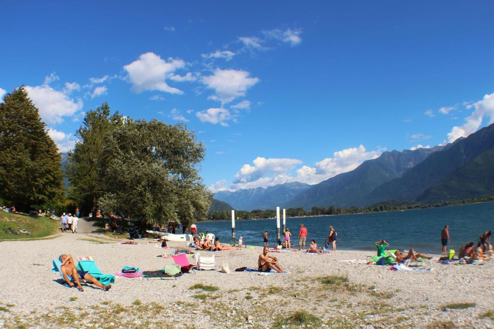 Strand mit Steinen, Menschen und Bergen im Hintergrund unter blauem Himmel.