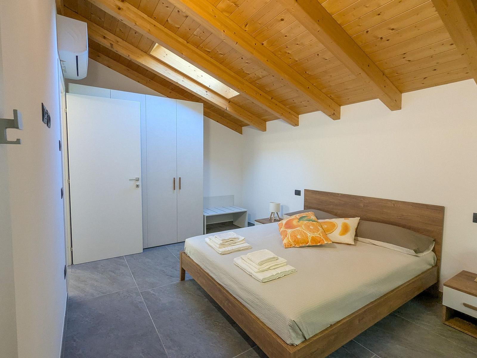 Schlafzimmer mit Holzdecke, Bett, Kleiderschrank und Bodenfliesen.