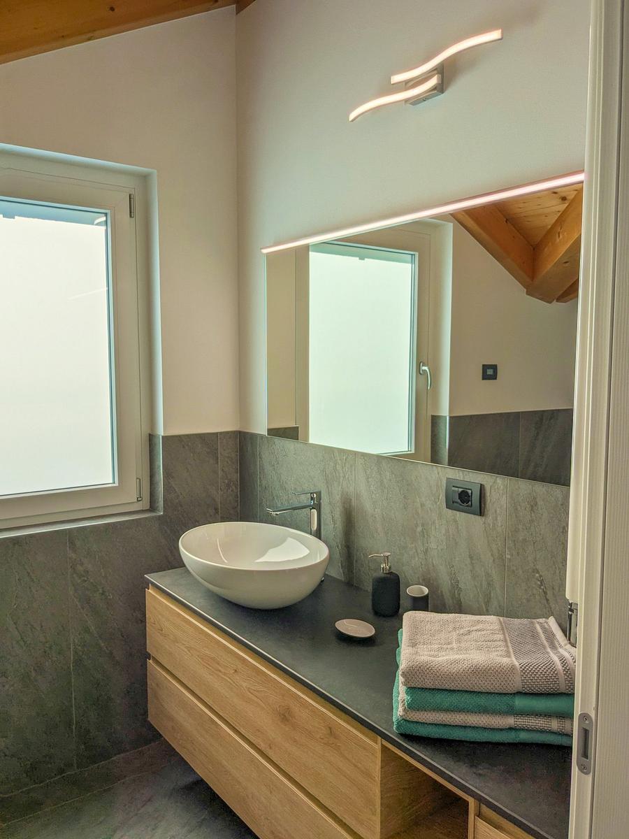 Badezimmer mit Waschtisch, Spiegel und Fenster. Holzdecke und gefaltete Handtücher.