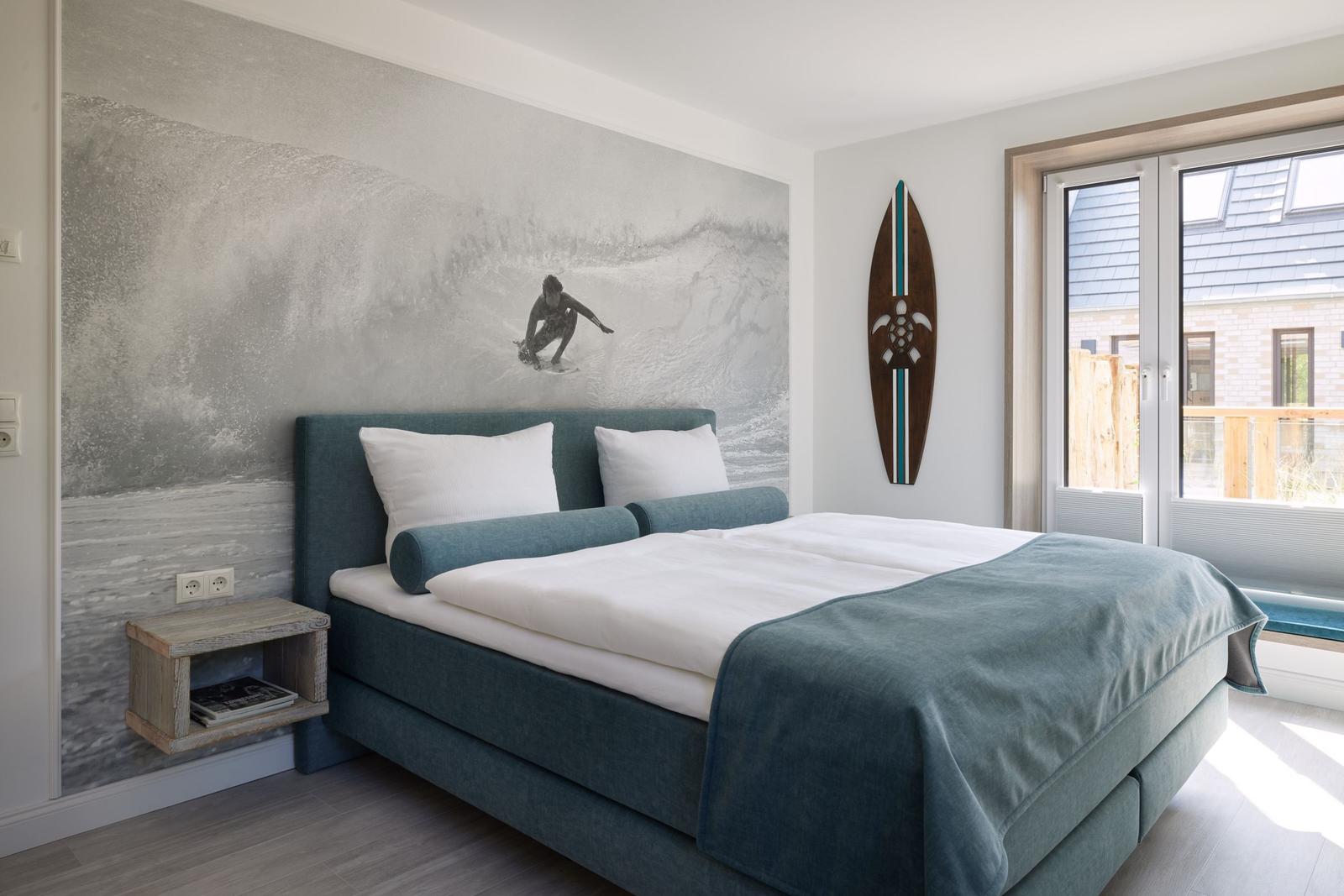Schlafzimmer mit Surf-Motivwand, Bett und Fenster zum Balkon.