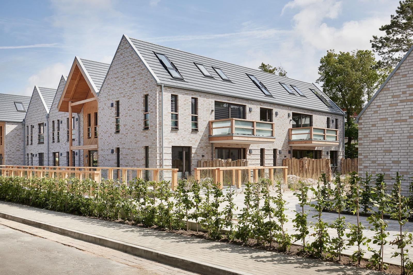 Moderne Wohnhäuser mit Holzverkleidung und Balkonen. Grünflächen und Gehwege im Vordergrund.