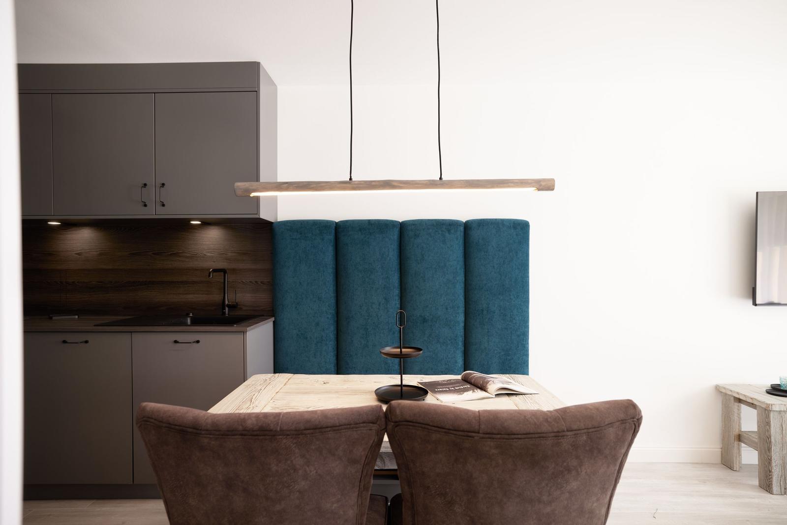 Essbereich mit Holztisch, blauer Sitzbank und moderner Küchenzeile.