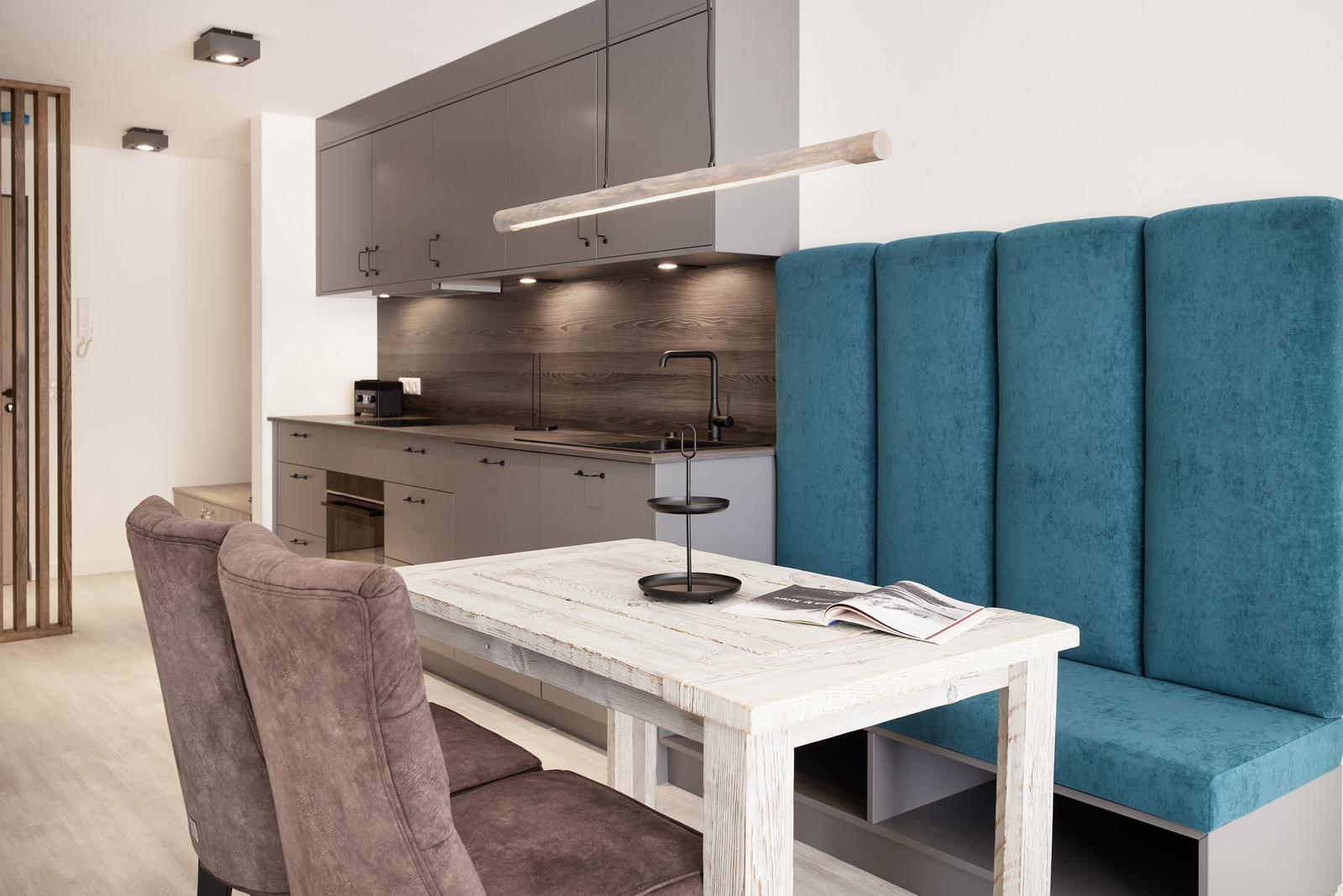 Essbereich mit Holztisch, blauer Sitzbank und moderner Küche im Hintergrund.