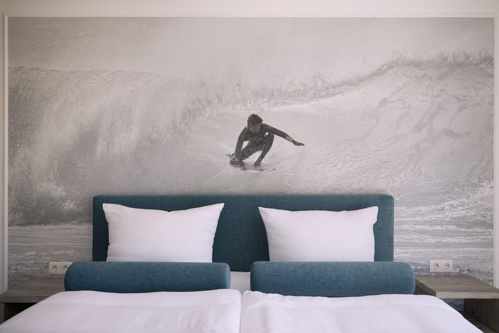 Schlafzimmer mit Bett und Wandbild eines Surfers auf Wellen.