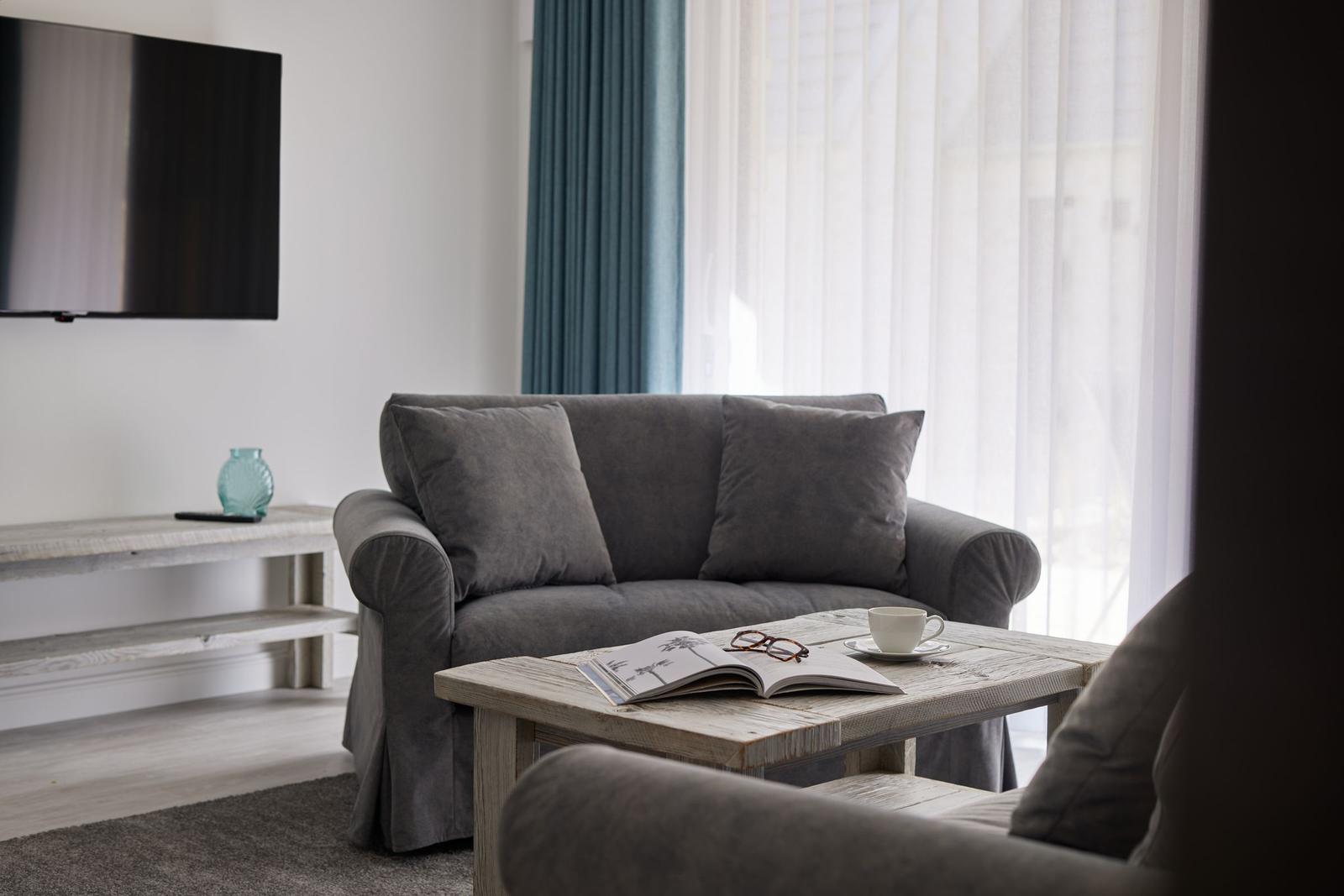 Ein Wohnzimmer mit grauem Sofa, Holztisch und Fernseher an der Wand.