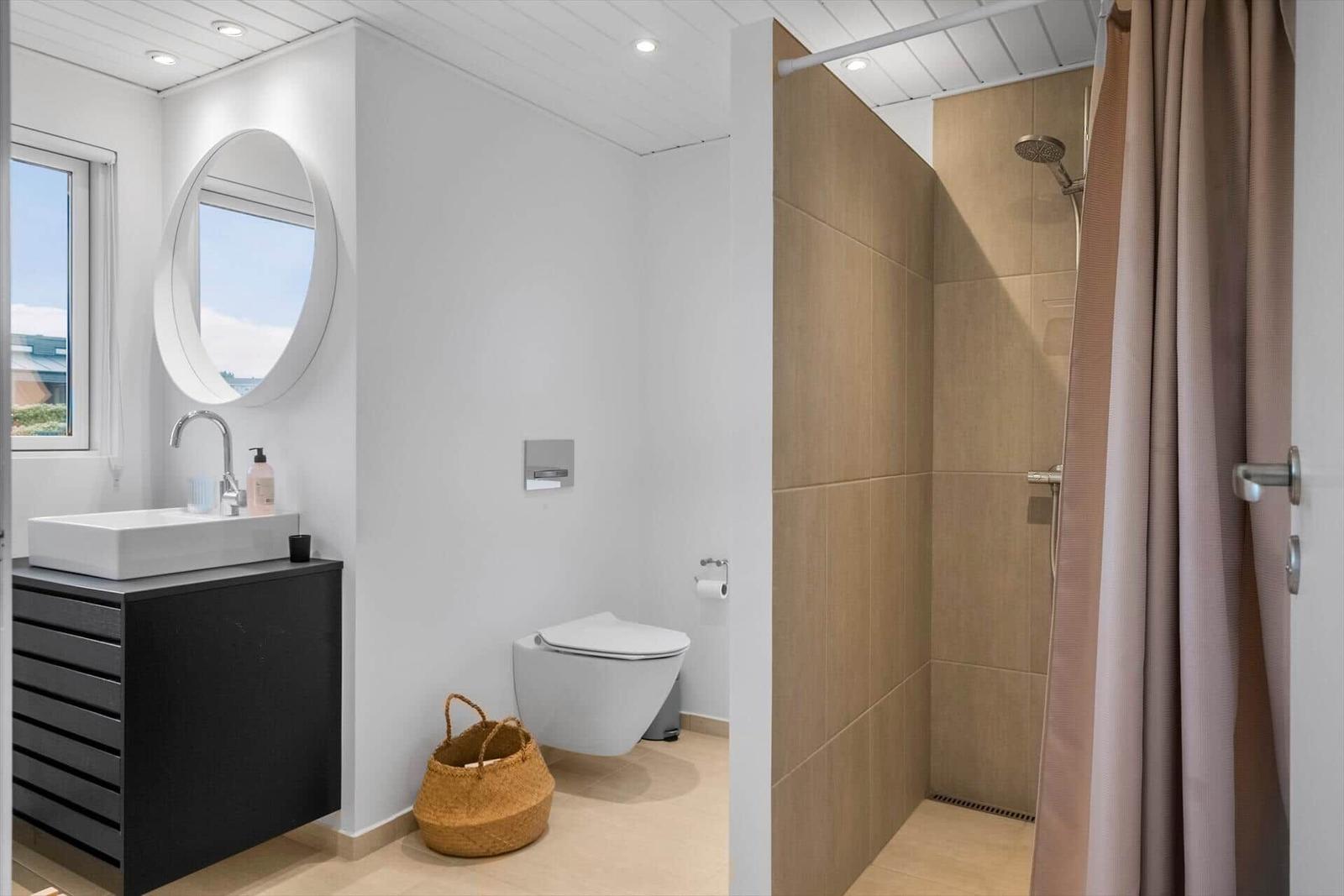 Badezimmer mit Dusche, Waschbecken und Toilette. Holzwand und runde Spiegel.