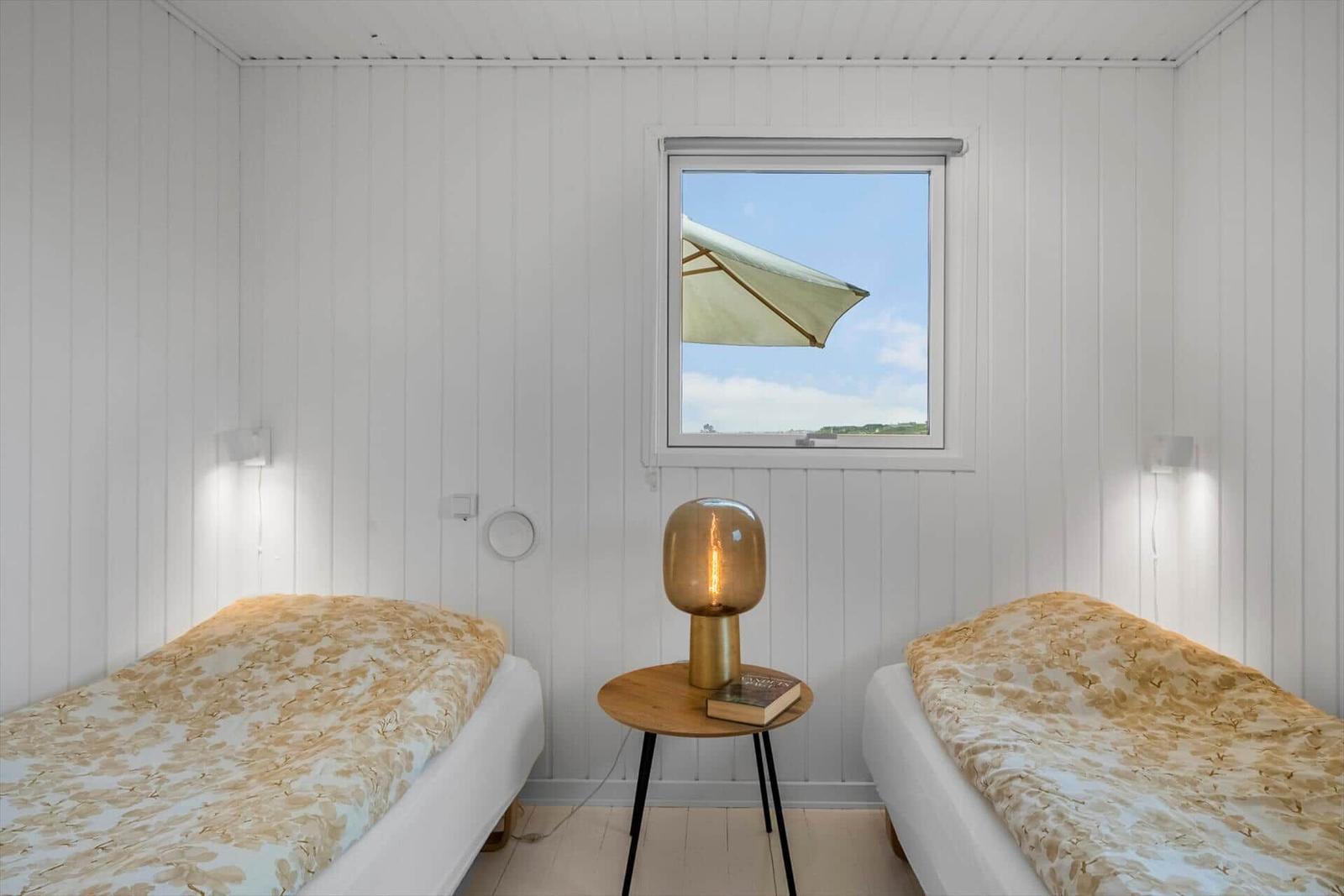 Zwei Betten mit gemusterten Bettdecken, ein Nachttisch mit Lampe und Blick auf eine Terrasse.