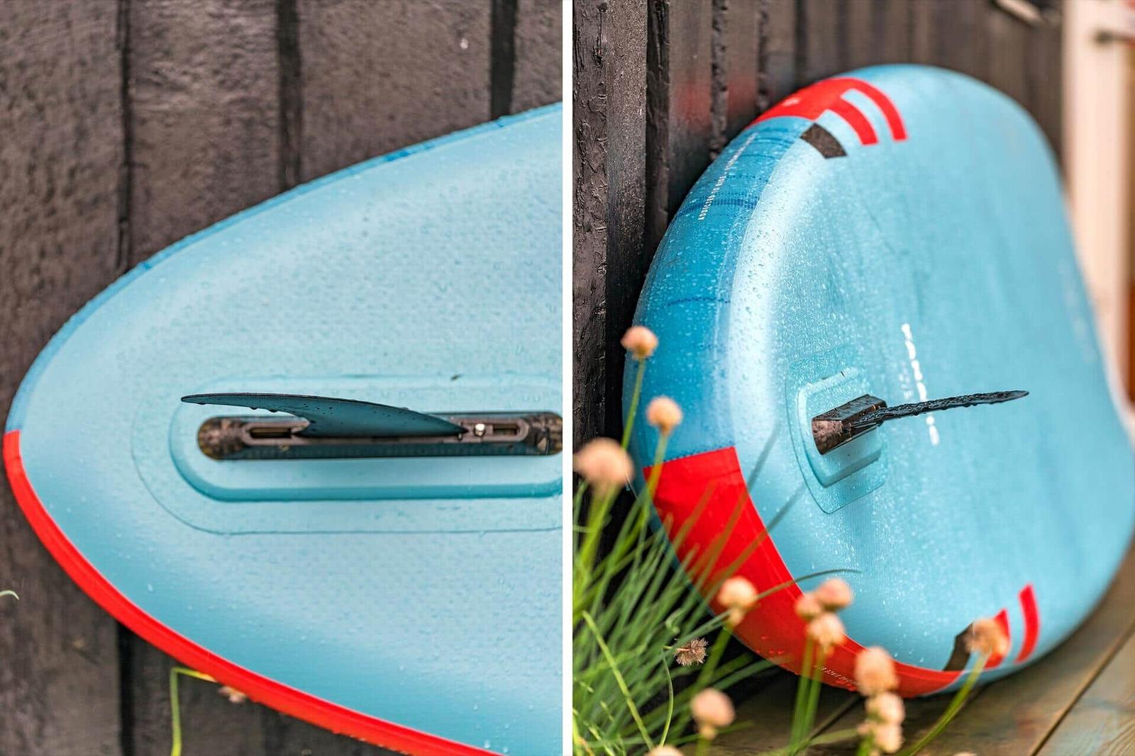 Blauer Stand-Up-Paddleboard mit rotem Rand lehnt an eine Holzwand.