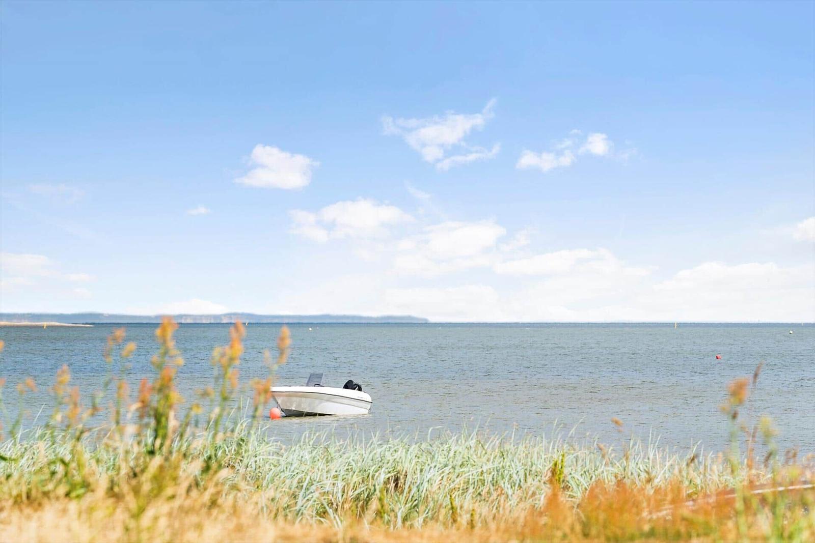 Ein weißes Boot liegt im Wasser vor einer Küstenlandschaft unter blauem Himmel.
