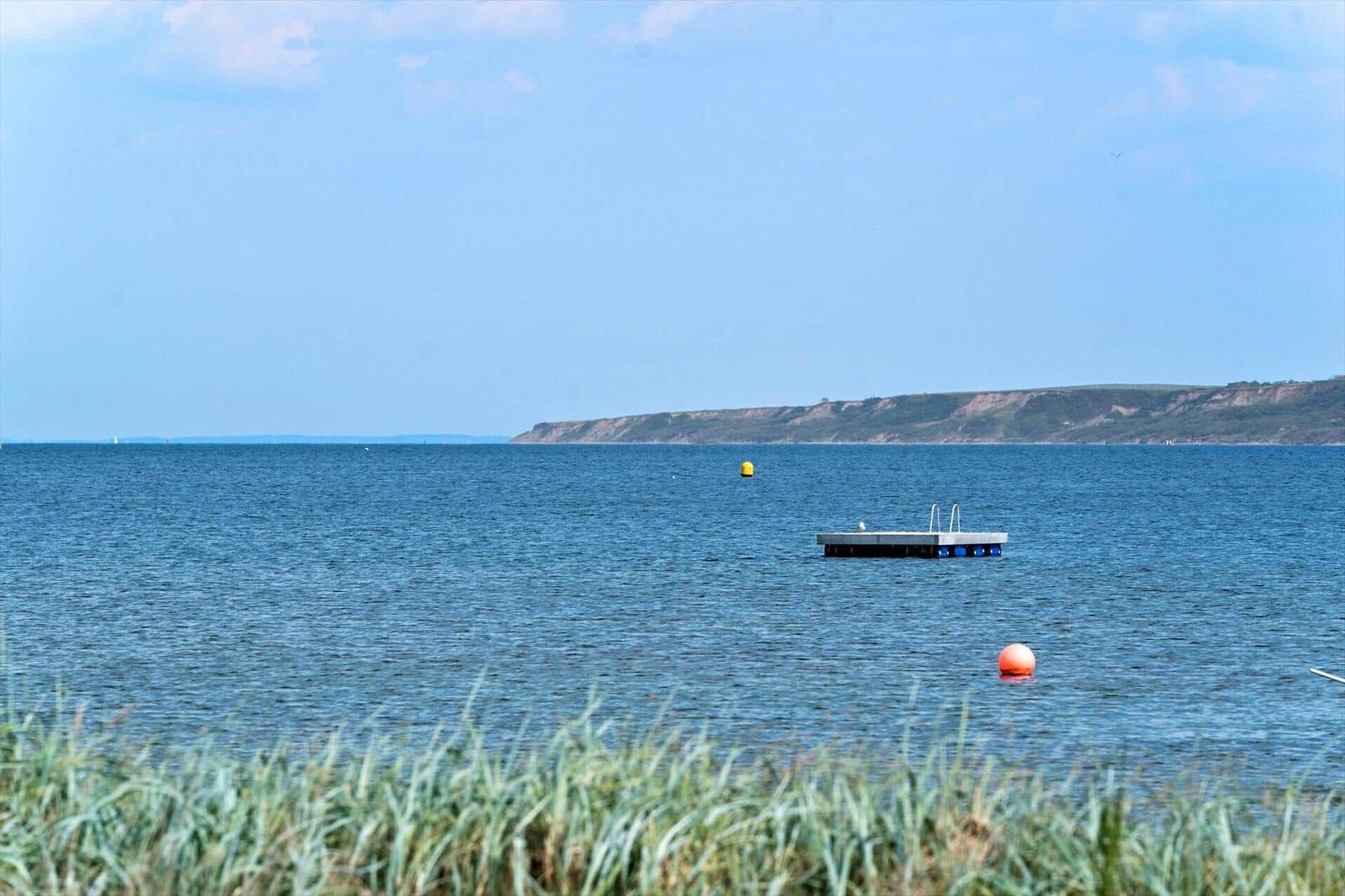 Ein schwimmender Steg mit Leitern im Wasser. Im Hintergrund Hügel und blauer Himmel.