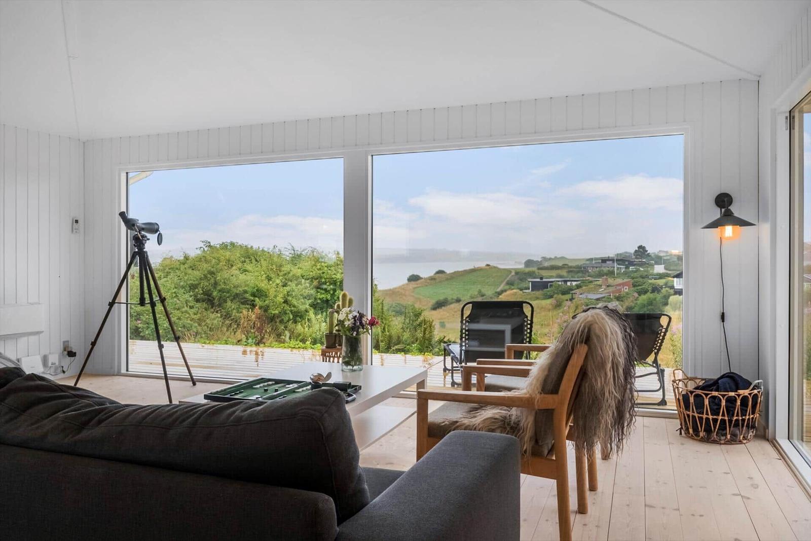 Wohnzimmer mit Blick auf Landschaft und See. Es gibt einen Sofa, einen Stuhl und ein Fernrohr.