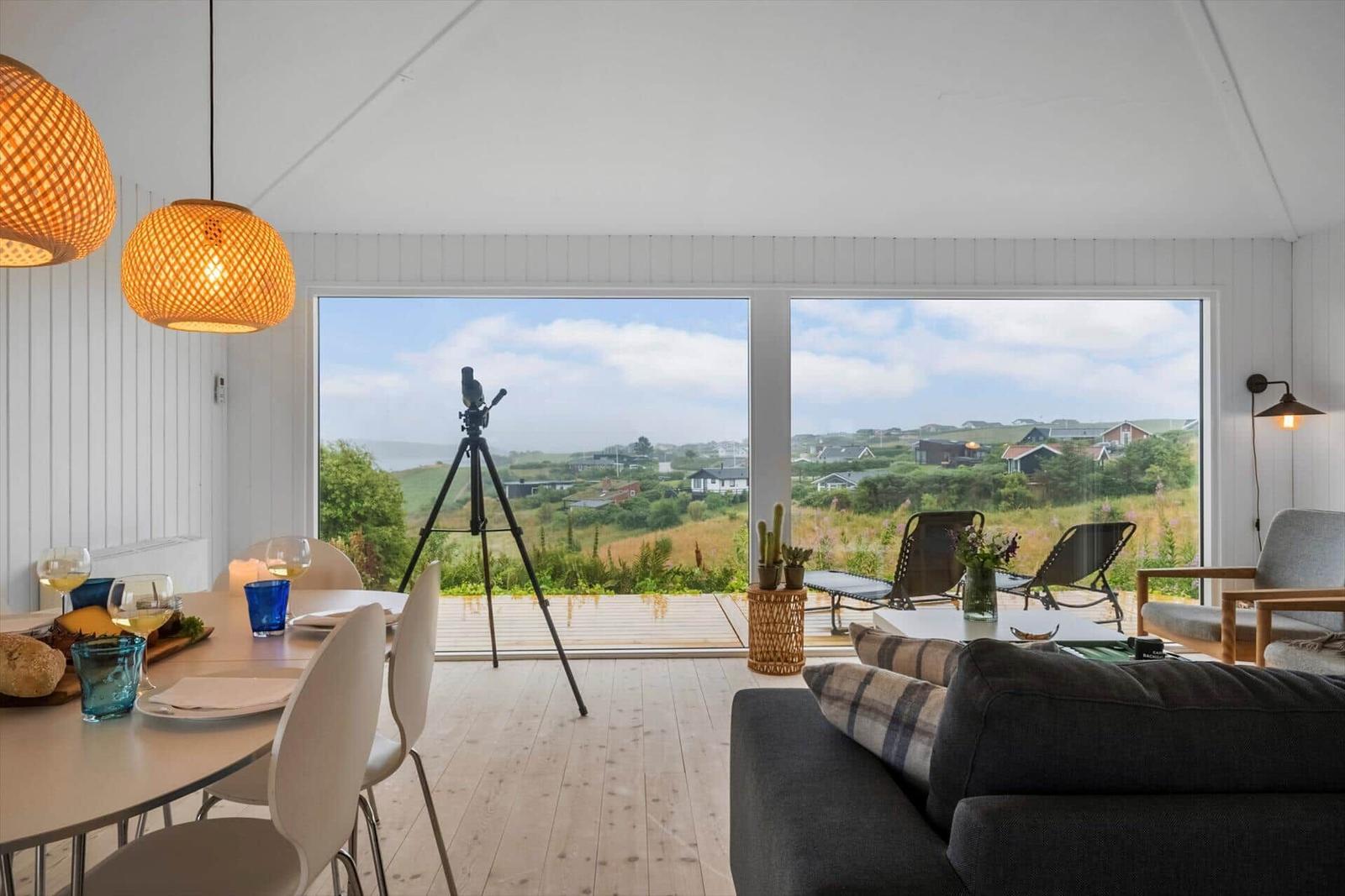 Wohnbereich mit Blick auf grüne Landschaft und Terrasse mit Liegestühlen.