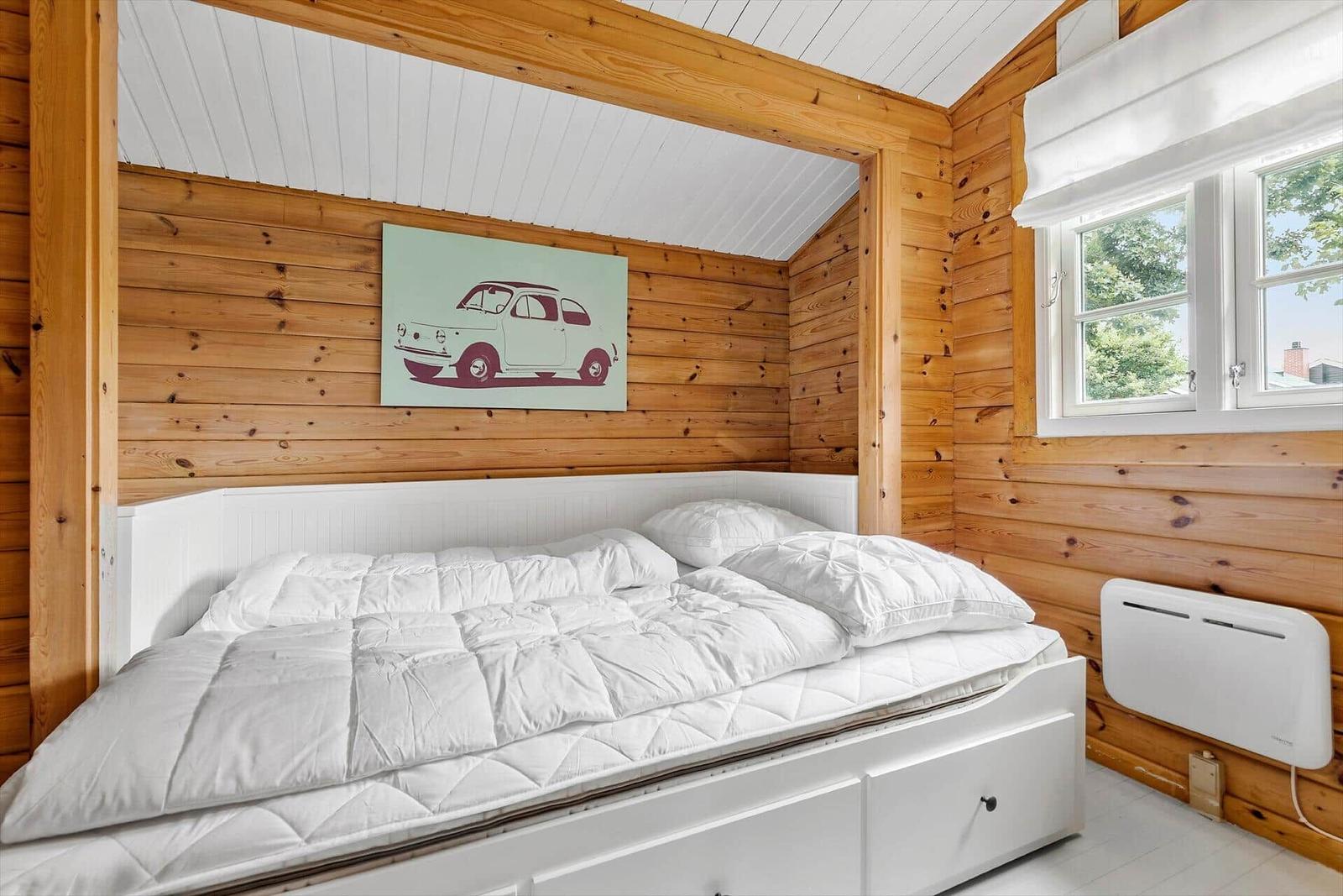 Bedroom with wooden walls, white bed, and window with view of trees.