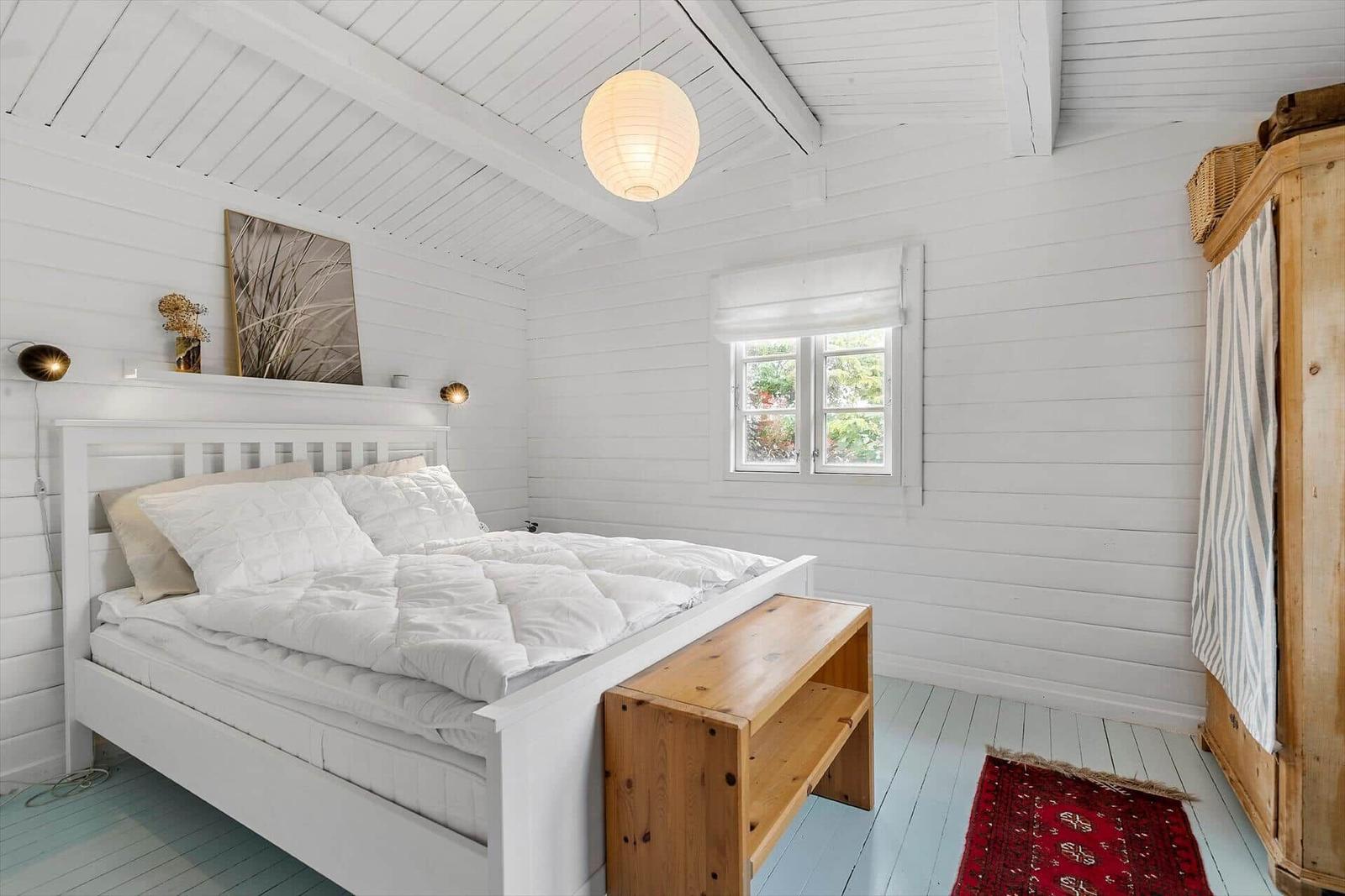 Bedroom with white bed, wooden bench, and window.