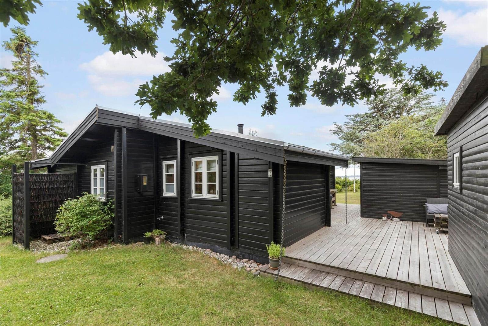 Black wooden house with deck and garden under trees