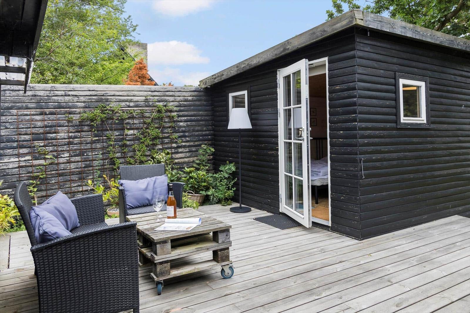 Black wooden cabin with open door and patio with seating area.
