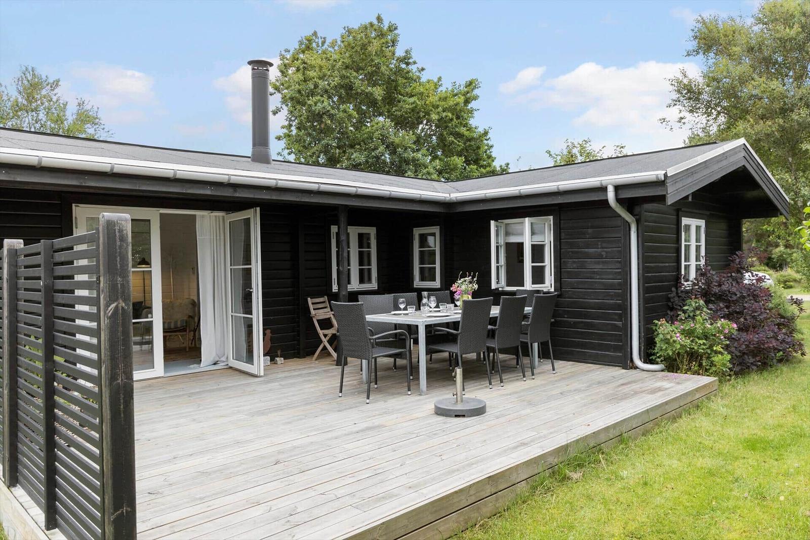 Black wooden house with terrace, table, chairs, and garden doors.