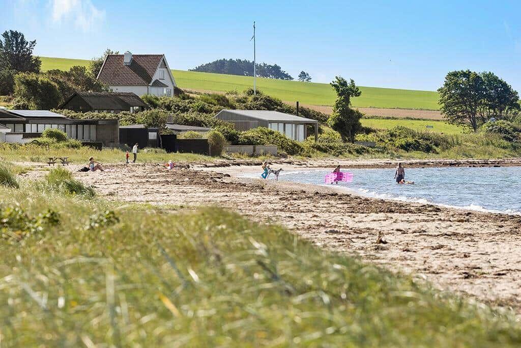 Beach with people, houses, and green slopes in the background.