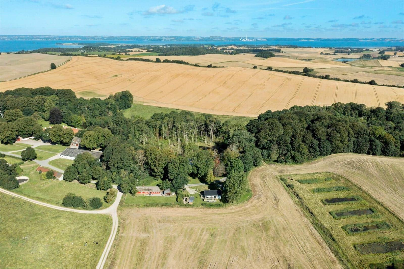 House in rural setting with fields and forest. View of water in the background.