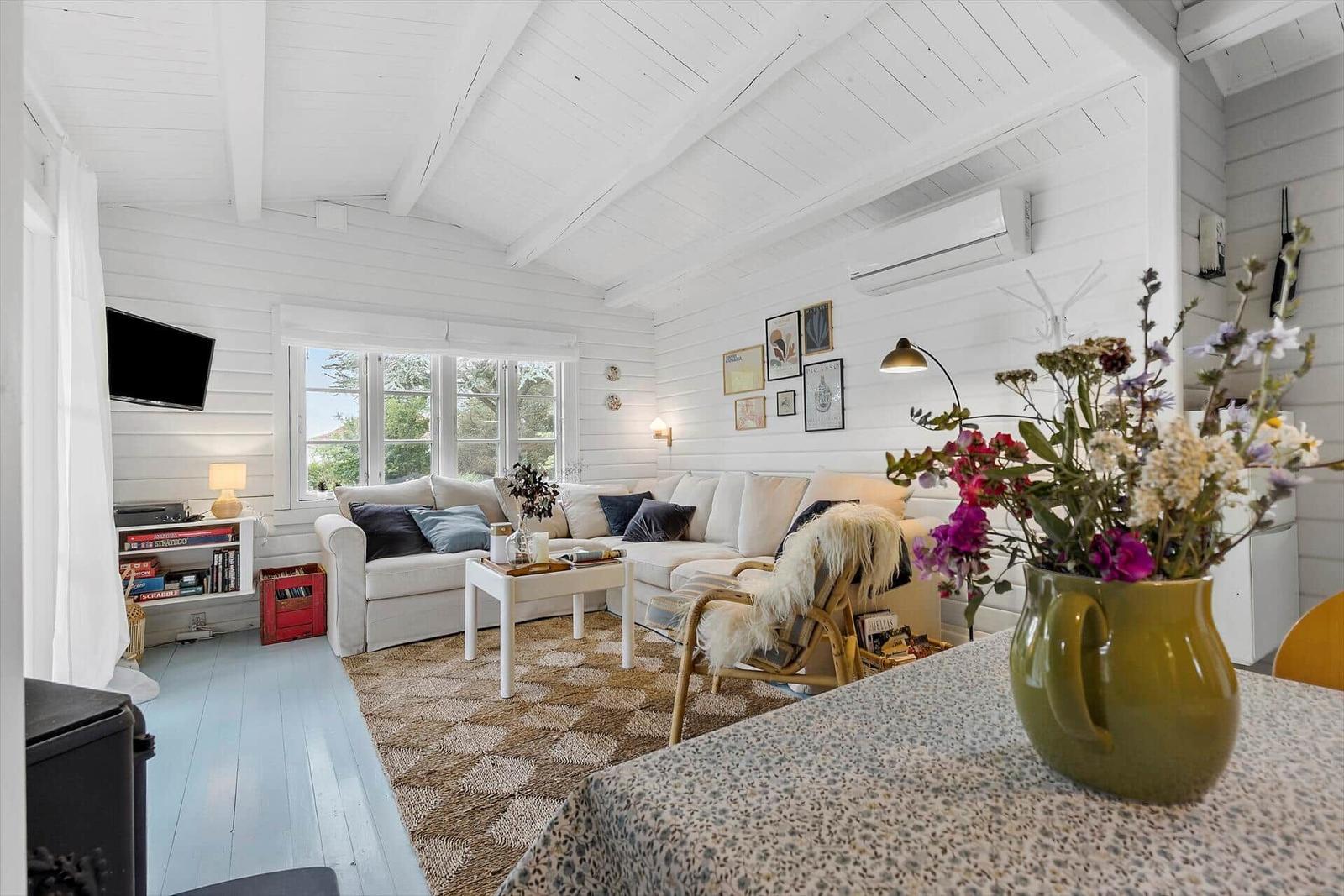 Living room with sofa, table, and window. Wall decor and flowers in the foreground.