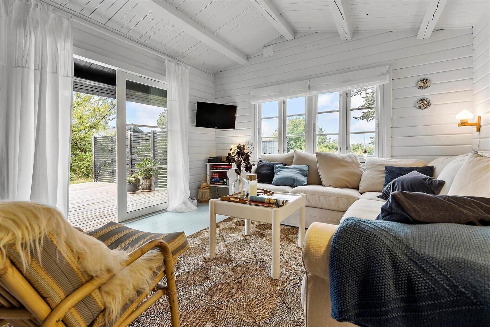 Living room with sofa, coffee table, and terrace. White wood walls and large windows.