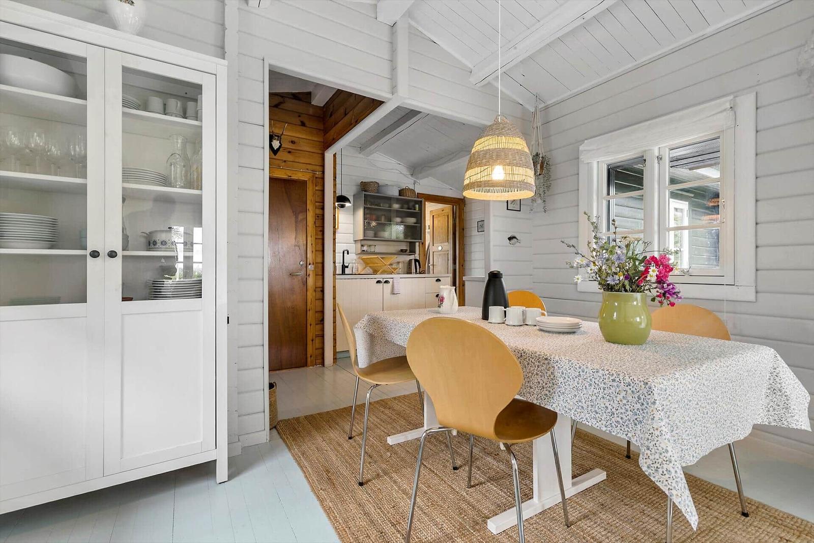 Dining area with table, chairs, and vase. Kitchen area in background.
