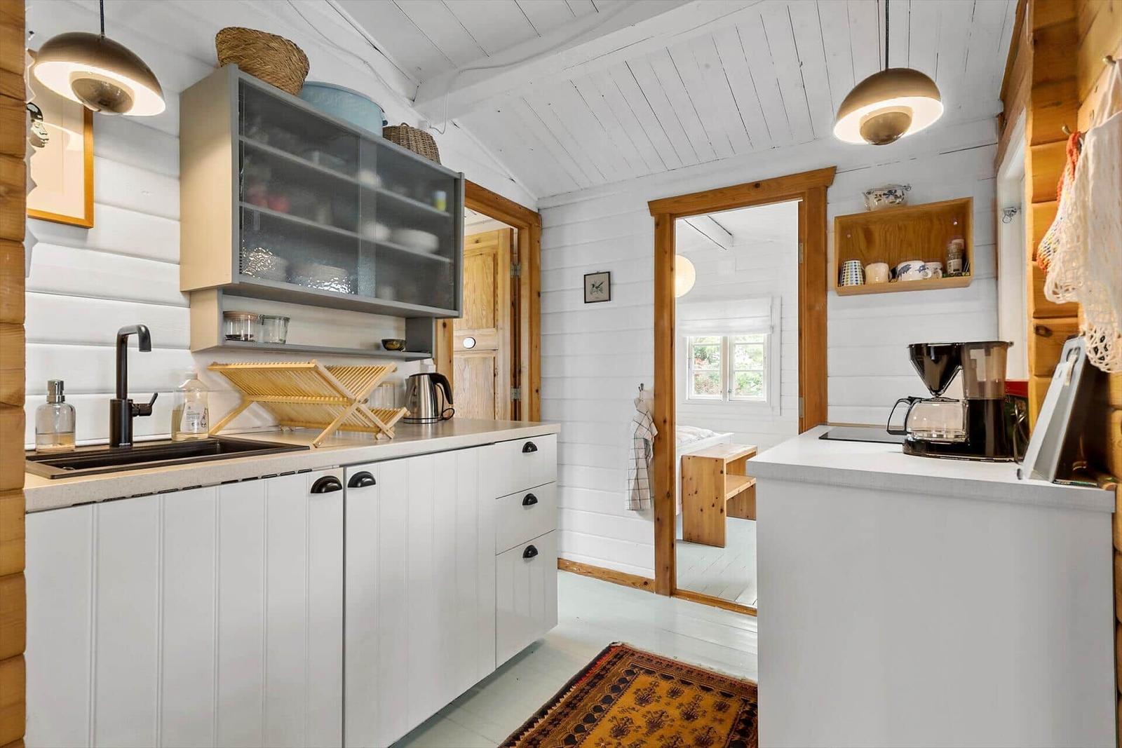 Kitchen with white cabinets and wooden ceiling. Passage to bedroom.