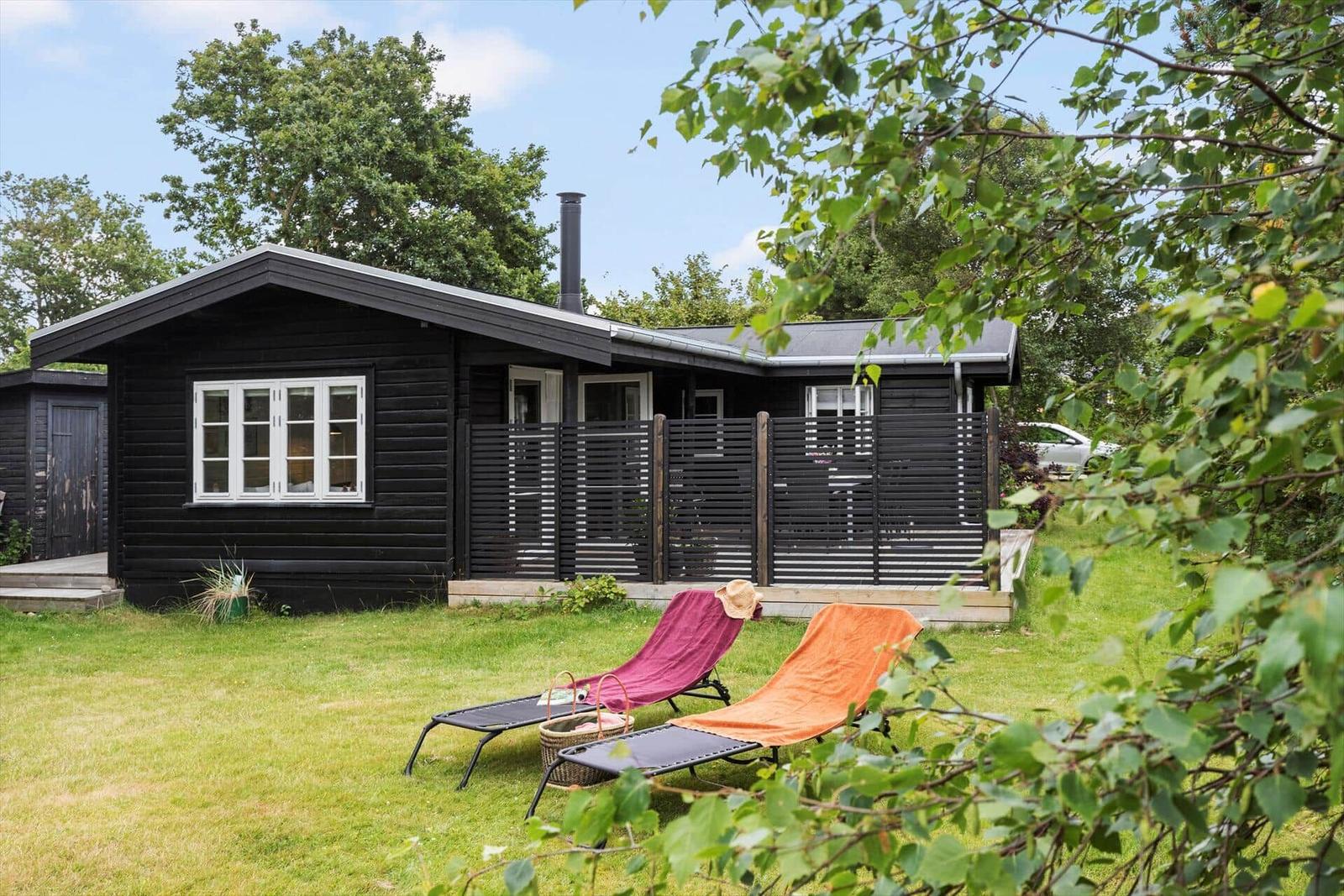 Black wooden house with balcony, garden loungers, and green lawn.