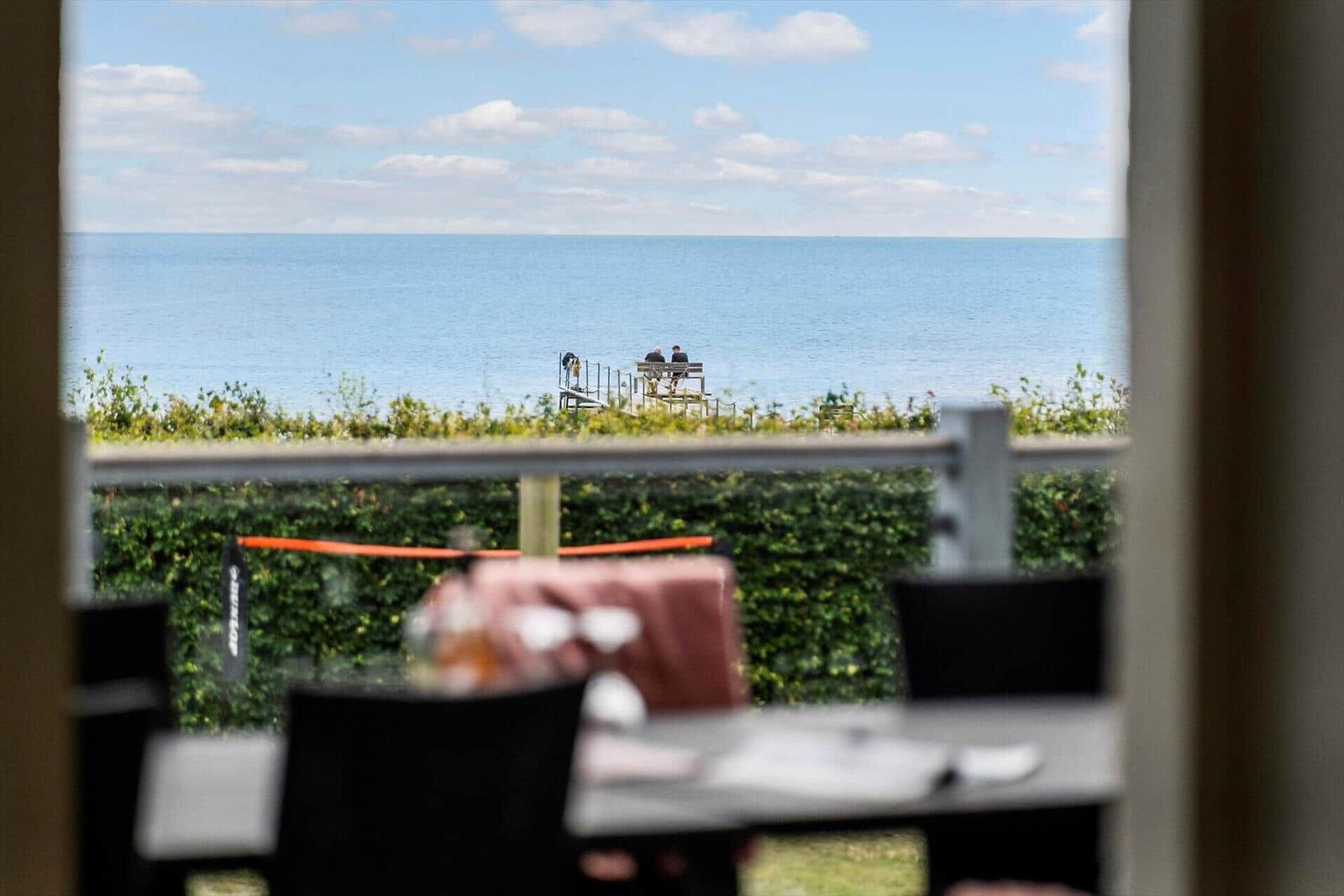 Aus dem Fenster blickt man auf das Meer und eine Terrasse mit Sitzgelegenheiten.