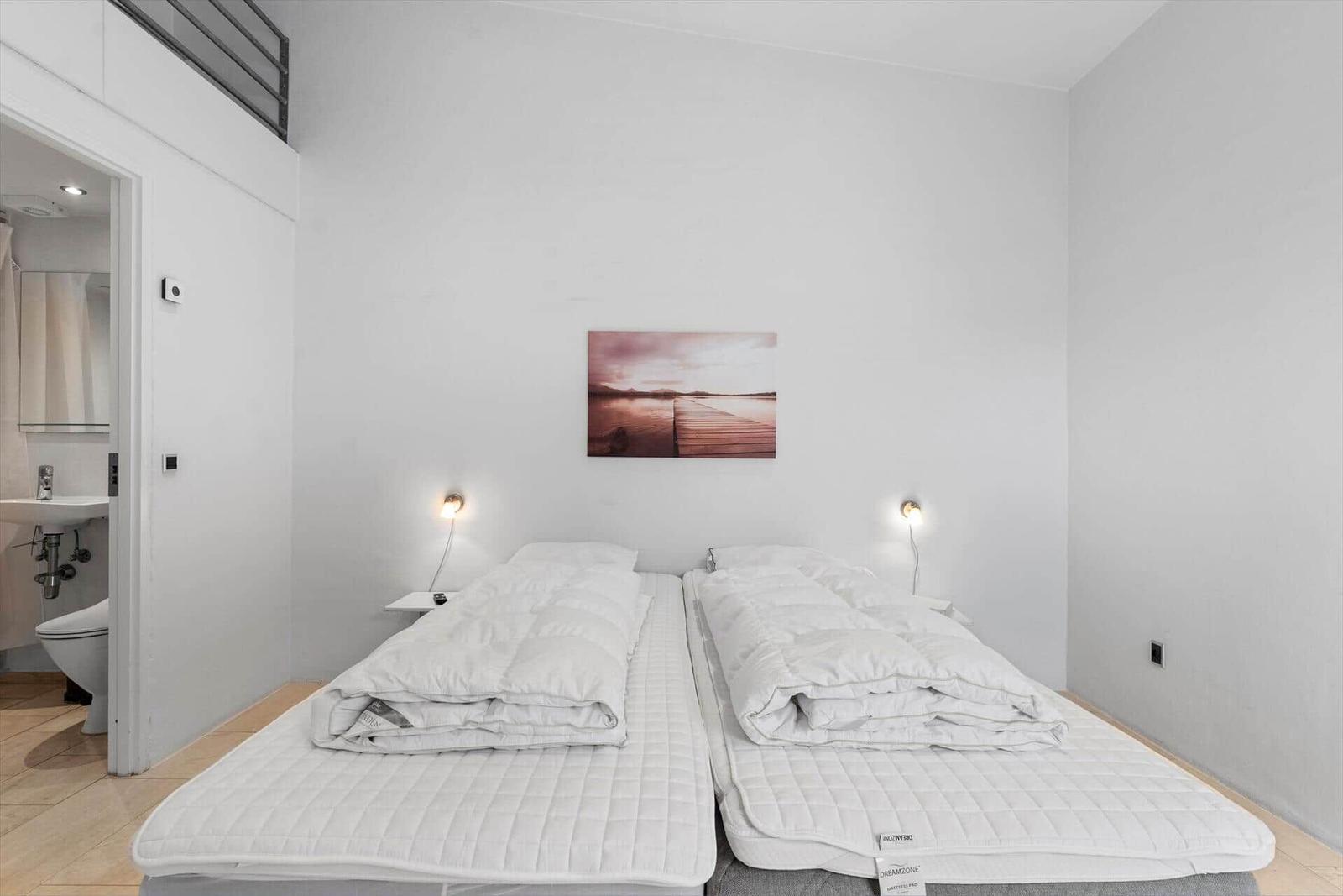 Zwei Matratzen mit weißen Decken, Wandbild und Nachttische mit Lampen.