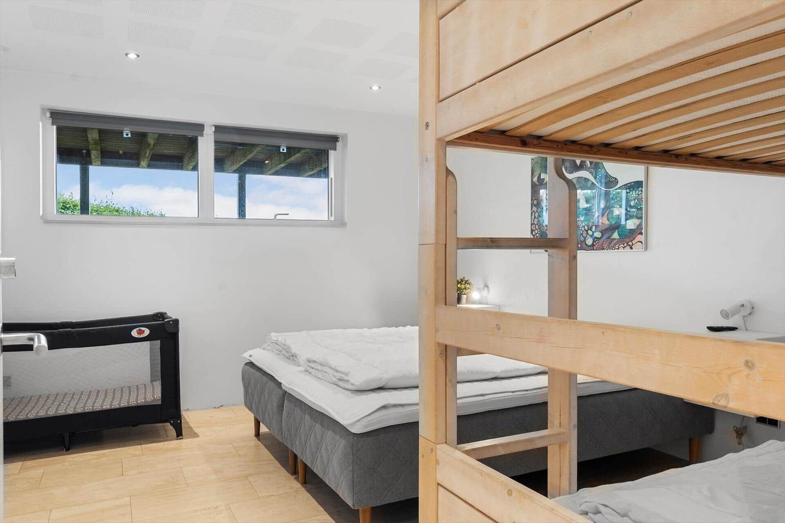 Zimmer mit Doppelbett, Krippe und Holz-Kojenbett. Fenster mit Blick auf Außenbereich.