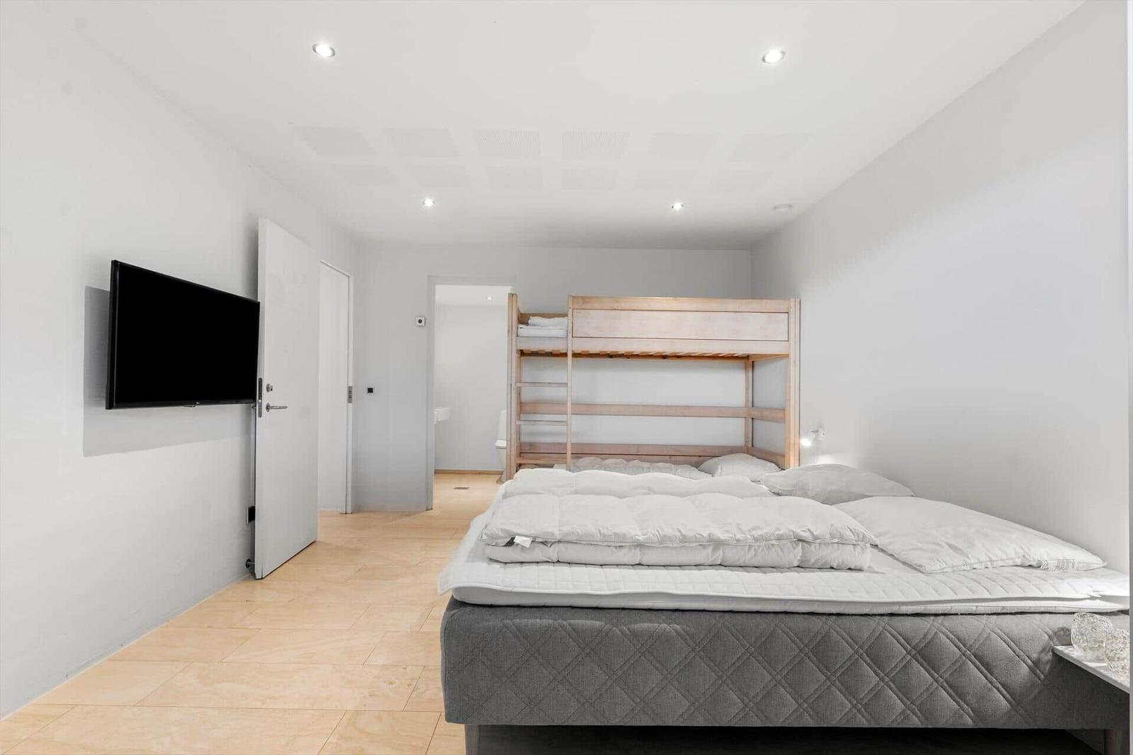 Schlafzimmer mit Doppelbett und Hochbett, Wand-TV und Holzboden.