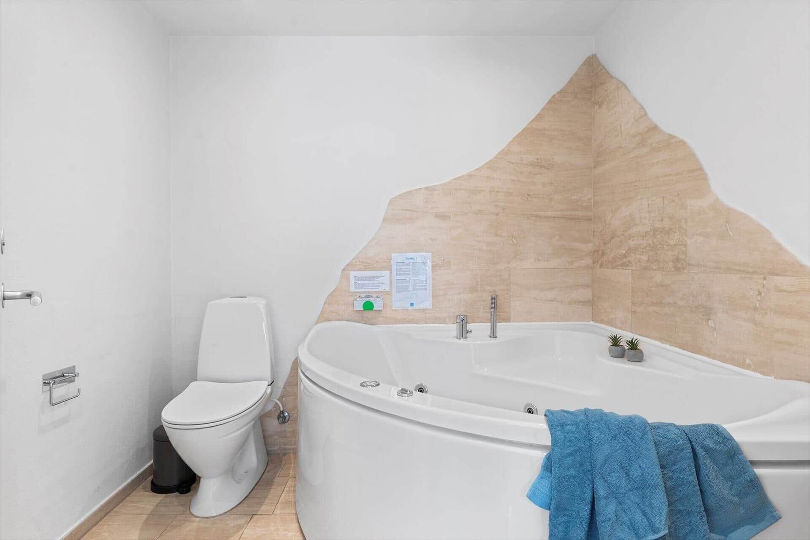 Bad mit Whirlpool, Toilette und Holzfliesen an der Wand.
