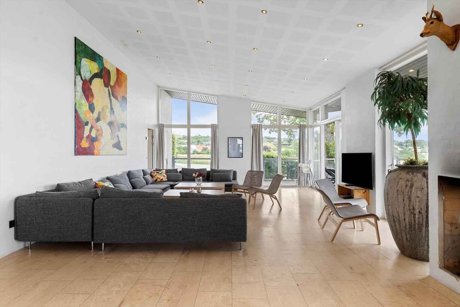 Großes Wohnzimmer mit grauem Sofa, großen Fenstern und moderner Einrichtung.