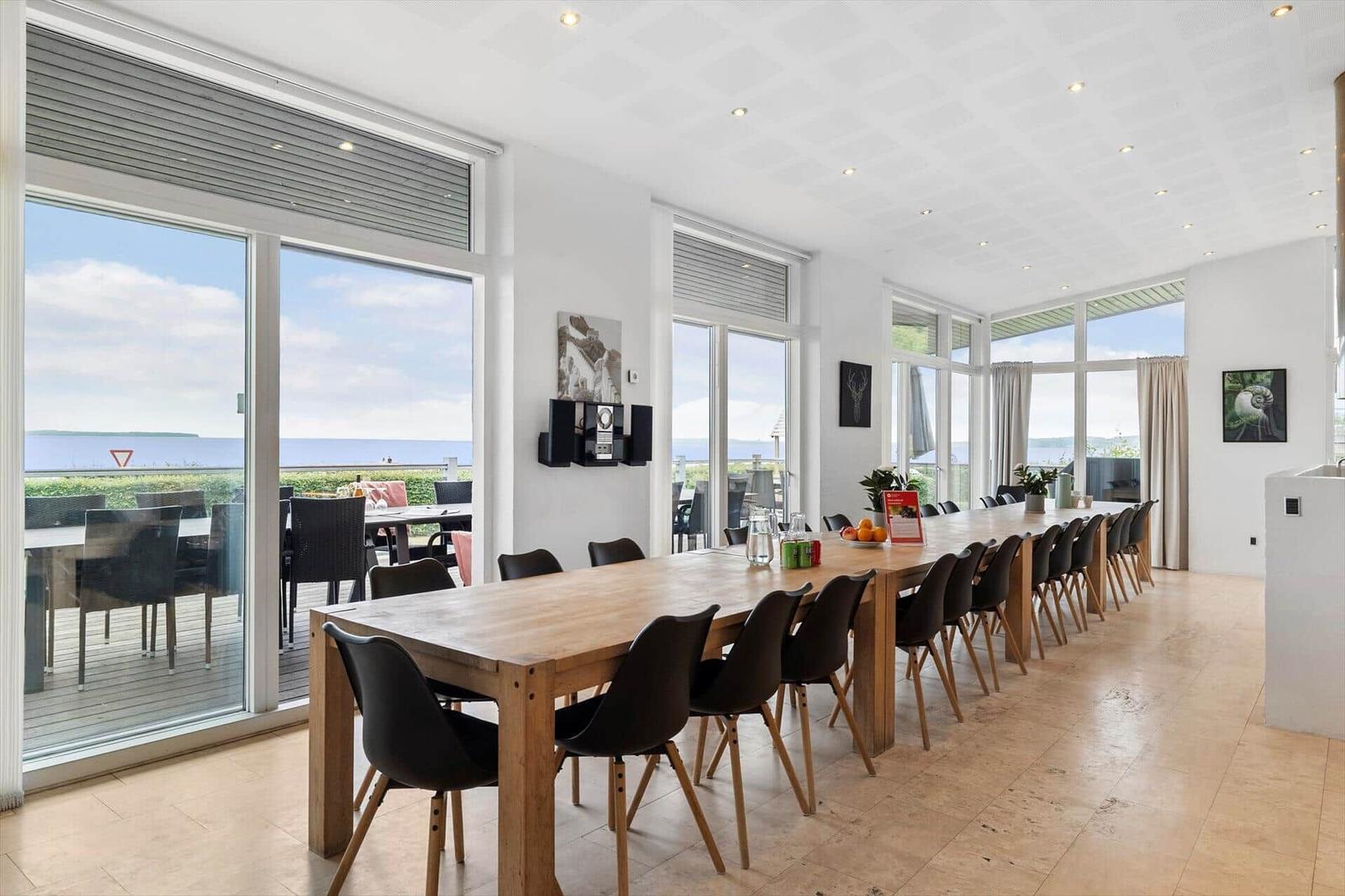 Großer Speisesaal mit Holztisch und Sitzgelegenheiten. Blick auf den See durch große Fenster.