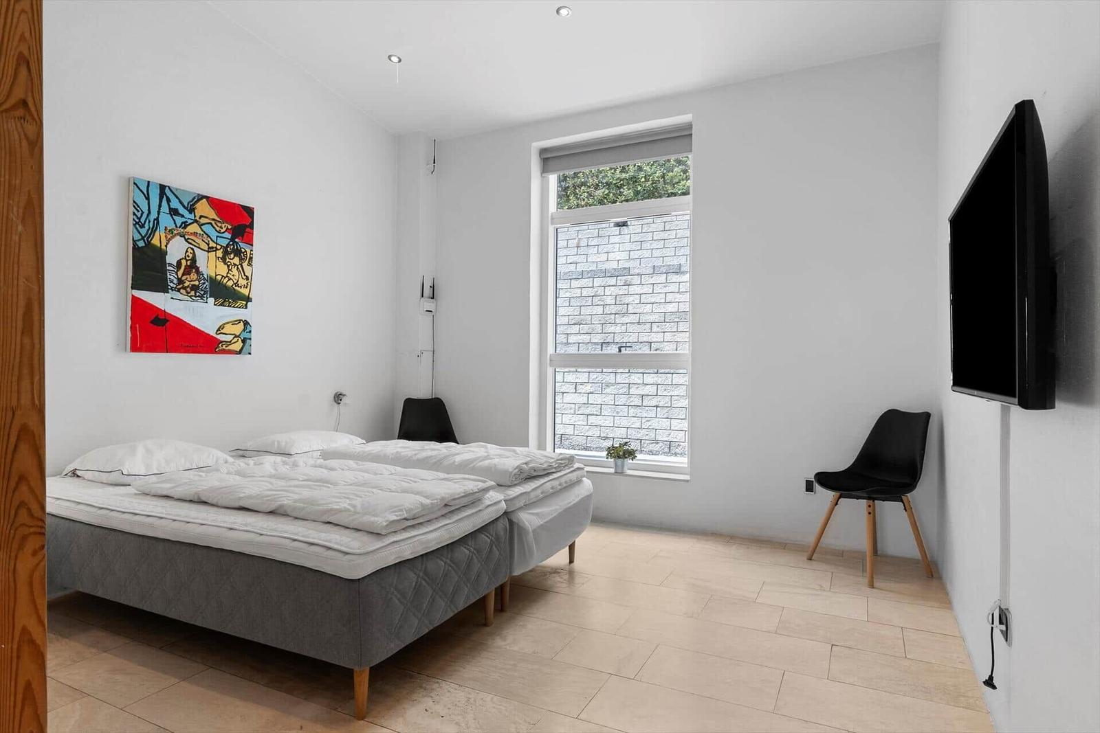 Zimmer mit Doppelbett, Fenster, Stuhl und Wandbild.