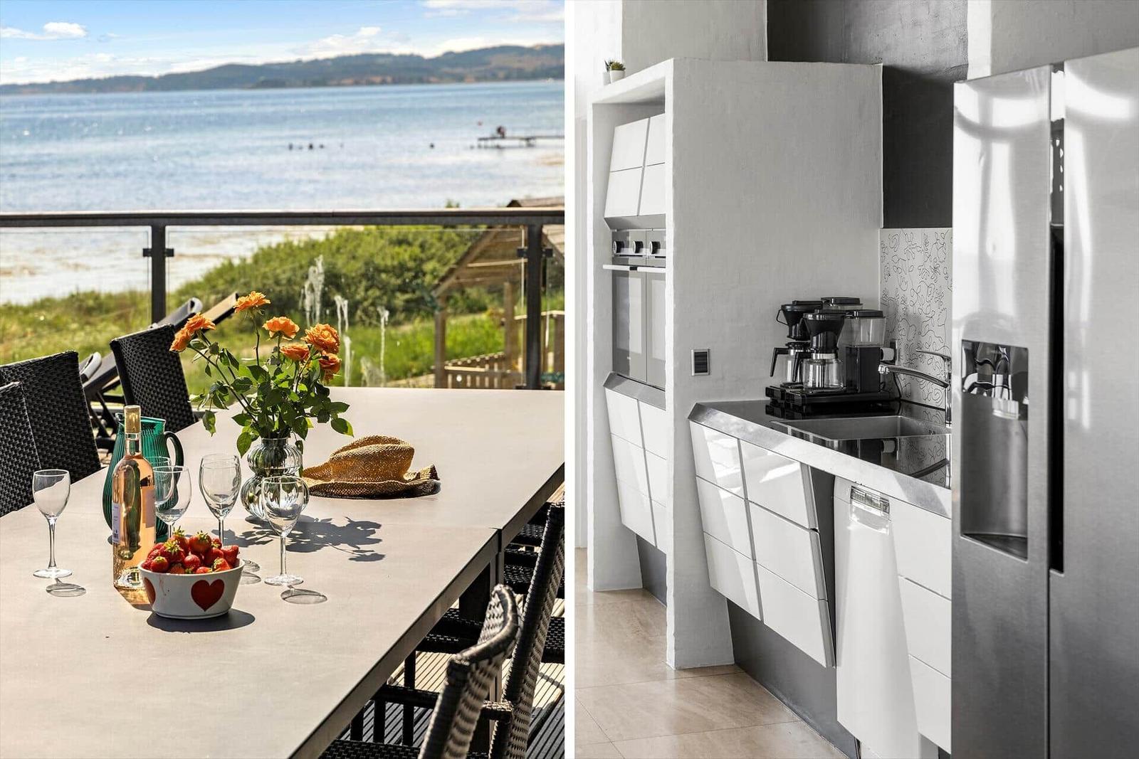 Terrasse mit Tisch, Stühlen und Blick auf Wasser. Küche mit weißen Schränken und Edelstahlgeräten.