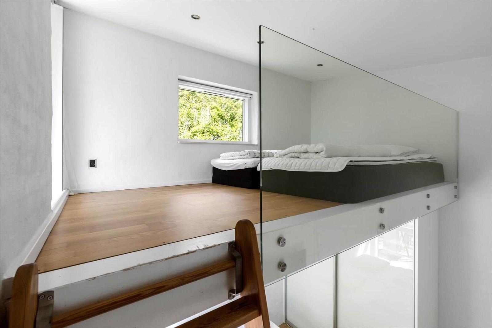 Hochbett mit Glasabtrennung und Holzboden. Fenster mit Blick auf Grün.