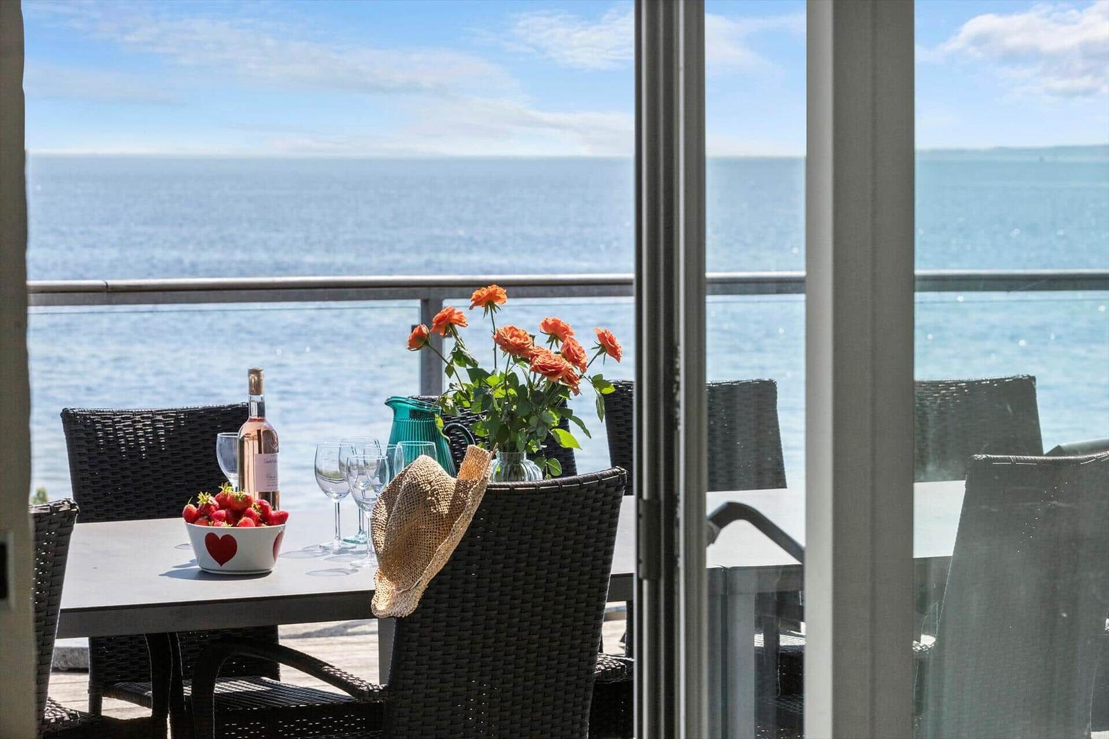 Terrasse mit Tisch, Stühlen, Blumen und Meerblick.