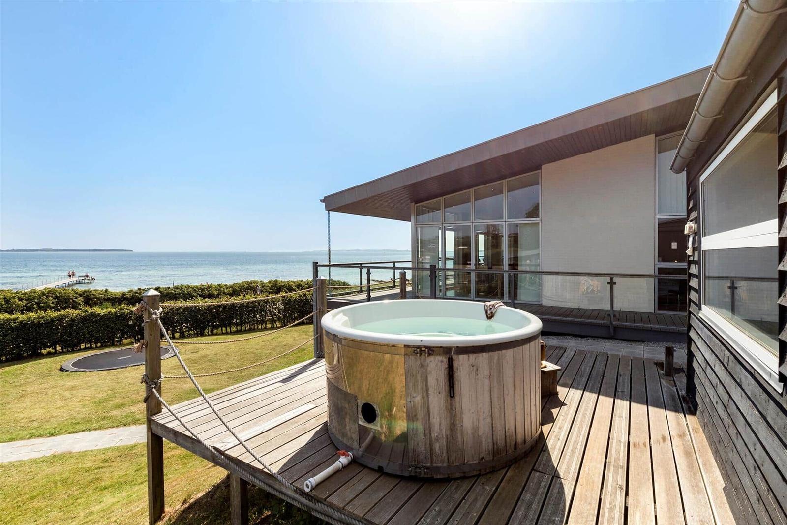 Haus mit Whirlpool auf Terrasse, Blick auf Meer und grünen Garten.