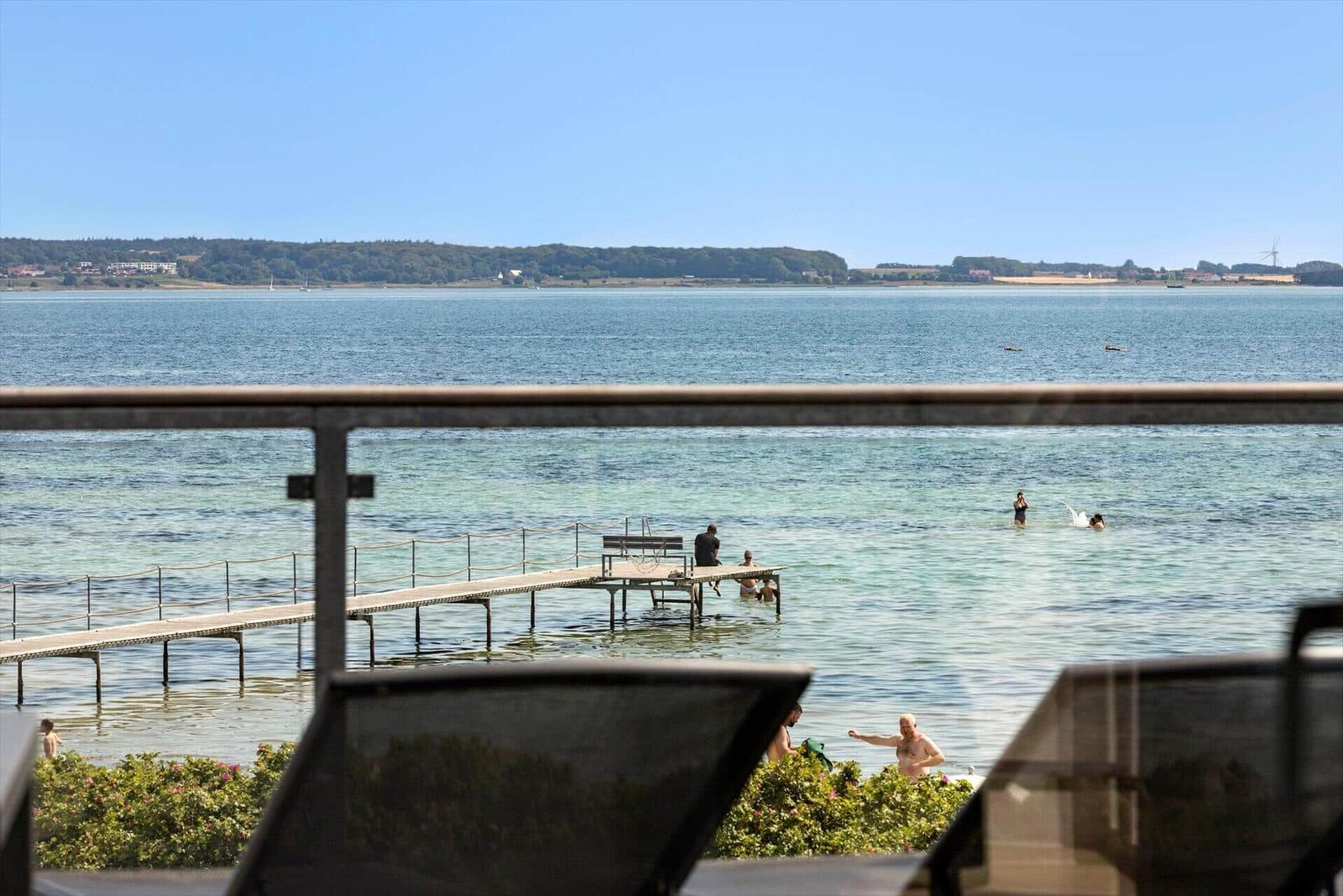 Blick von Balkon auf See mit Steg und Badegästen.