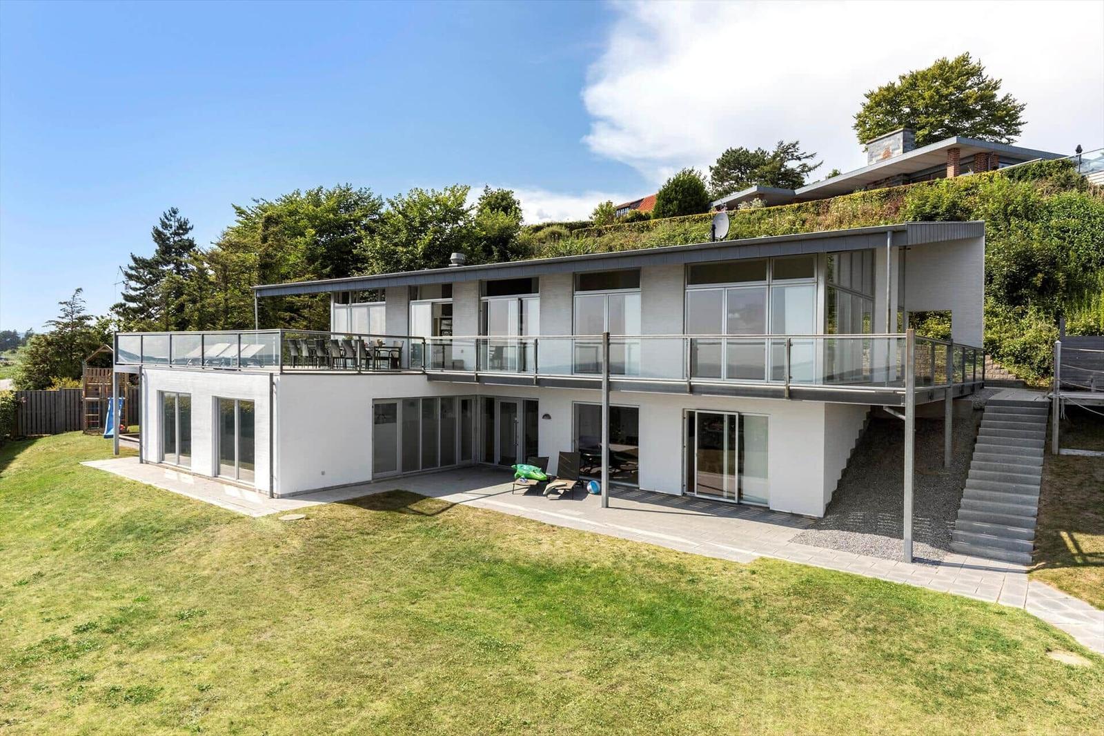 Moderne Villa mit Balkon, Terrasse und Grünfläche. Sicht auf Wald und Himmel.