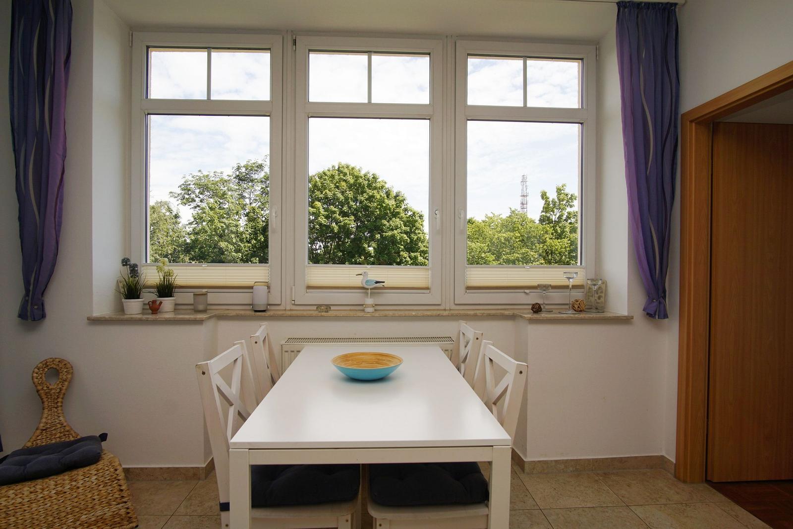 Essbereich mit weißem Tisch, Stühlen und Blick auf Bäume.