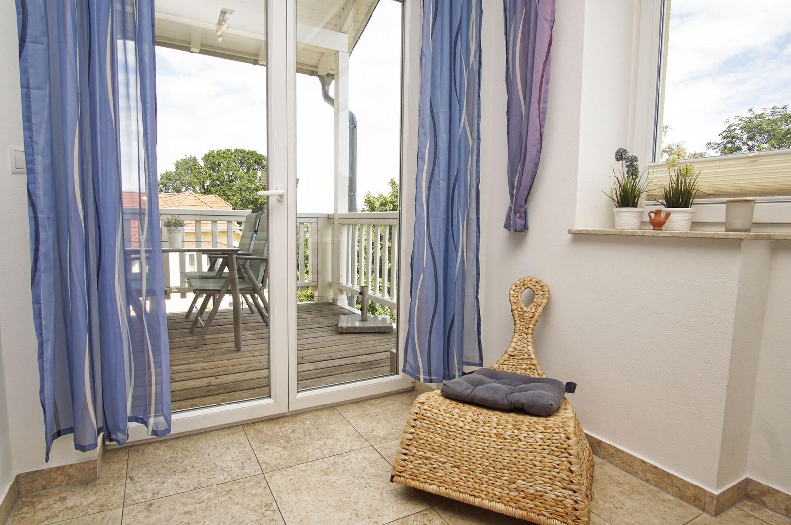 Terrassentür mit blauen Vorhängen führt auf eine Holterrasse mit Tisch und Stühlen.