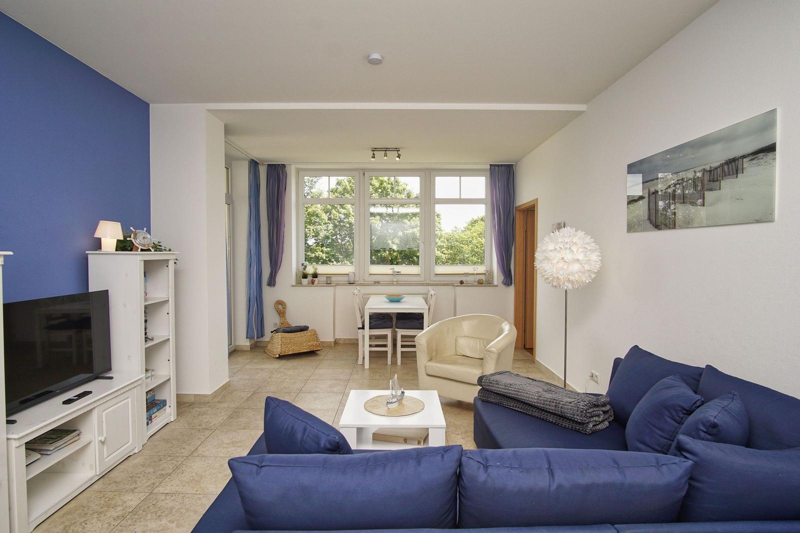 Wohnzimmer mit blauem Sofa, TV und Essbereich mit Tisch und Stühlen.