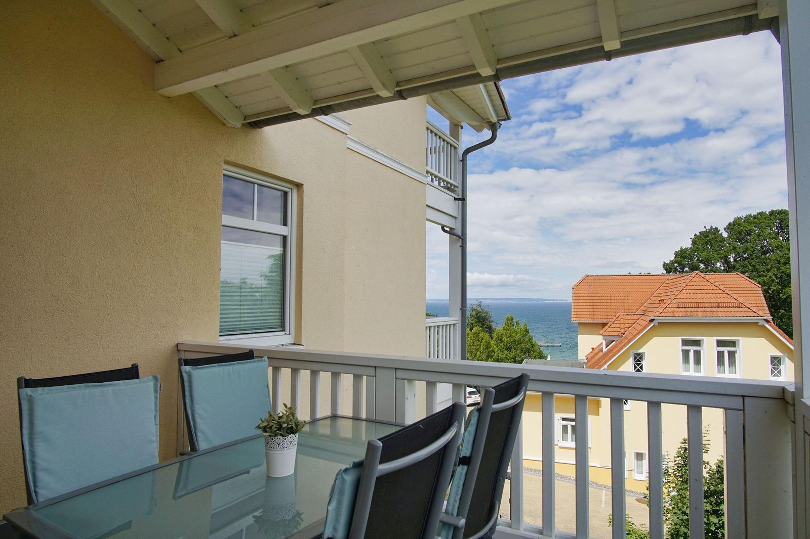 Terrasse mit Tisch und Stühlen. Blick auf das Meer und ein Haus.