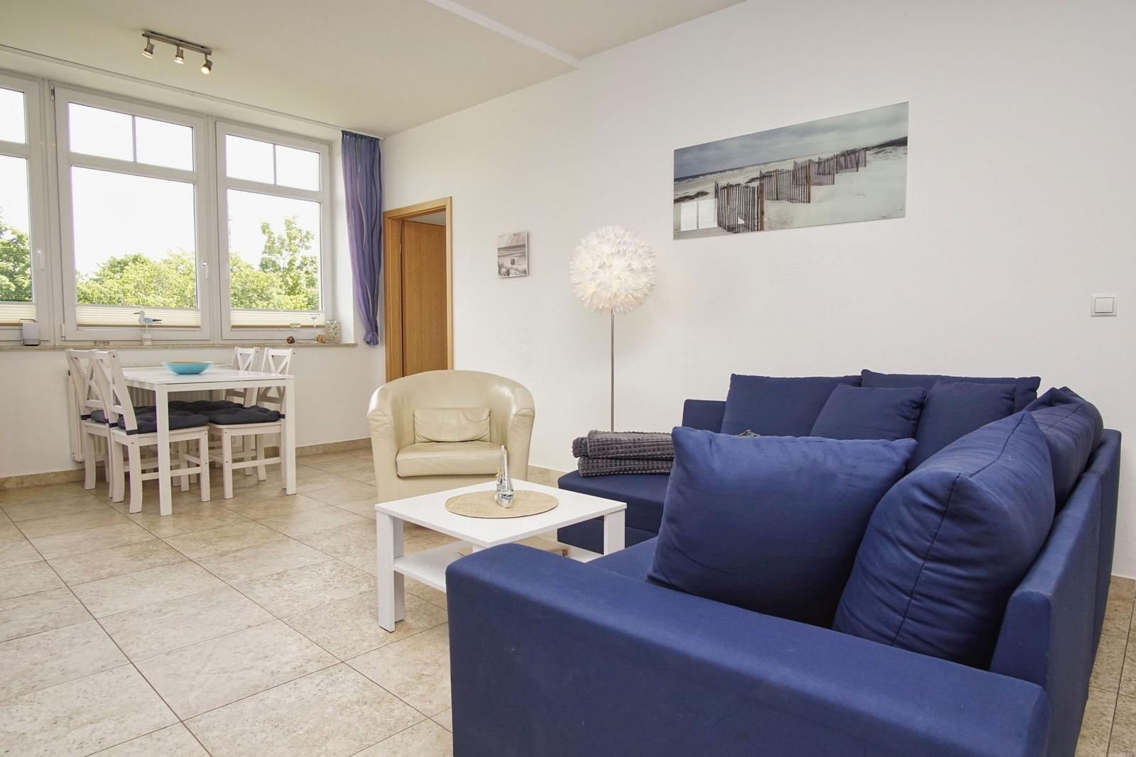 Wohn- und Essbereich mit Sofa, Tisch und Stühlen. Fenster mit Blick auf Grün.